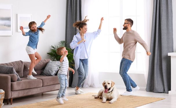 幸せなエネルギッシュな家族の完全な体:かわいい疲れた犬が家で週末にカーペットの上で休んでいる間に楽しさとダンスをしている両親と子供 - 写真・画像