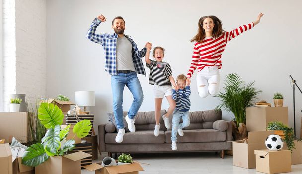 Полностью удовлетворенная семья: мужчина и женщина держатся за руки детей и прыгают на диване рядом с коробками во время переезда в новую квартиру - Фото, изображение