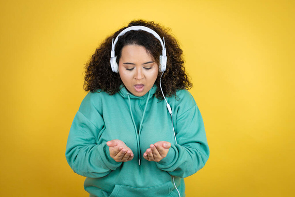 Young african american girl wearing gym clothes and using headphones Smiling with hands palms together receiving or giving gesture. Hold and protection - Photo, Image