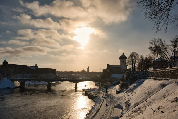 Winterliche Stadtlandschaft, Gegenlicht, links die Festung Ivangorod, rechts die Burg Narva und in der Mitte in der Ferne die Silhouette der Großen Alexander-Kirche von Narva. - Foto, Bild