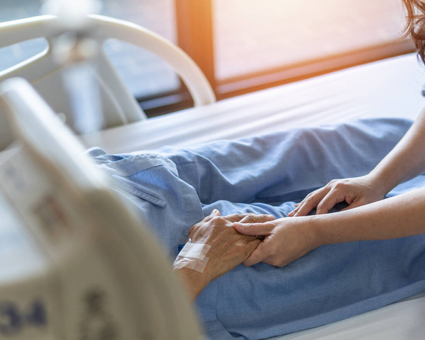 Opiekun i starszy pacjent (w podeszłym wieku dorosły) trzymający się za ręce w szpitalnym łóżku lub hospicjum pielęgniarskim, geriatryczny dom paliatywny, podczas gdy opiekun mający opiekę medyczną - Zdjęcie, obraz