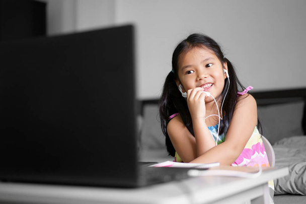Aziatisch kind of kind meisje glimlach genieten van e-learning en spreken tot een praatje op de computer notebook met het dragen van een koptelefoon voor studie online communicatie of leren van thuis en spelen laptop voor terug naar school - Foto, afbeelding