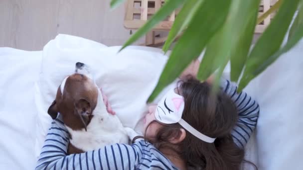4k. mała dziewczynka i uroczy pies chihuahua w masce oczu śpi w białym łóżku.  - Materiał filmowy, wideo