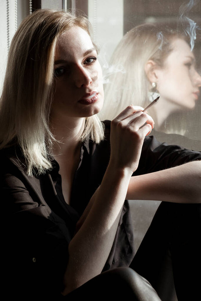 Primer plano de mujer joven fumando cigarrillo por la ventana - Foto, Imagen
