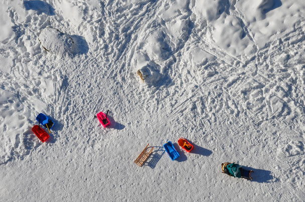 kilátás a havas síkság fa park padok és több szánok és műanyag gyermekek bobogó öröm egy téli napsütéses nap alatt egy kilátó emberek nélkül, lábnyomok útvonal - Fotó, kép