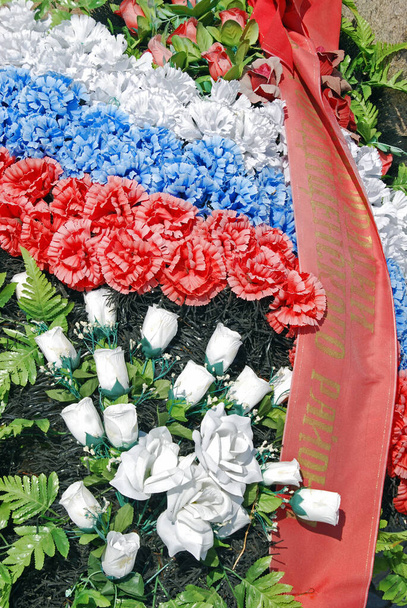 Vörös, fehér és kék virágok közelsége egy háborús emlékműre helyezve Volgogradban, Oroszországban. - Fotó, kép