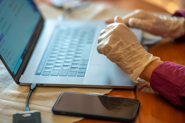 Man using laptop computer at home wearing gloves in pandemic time, detail on hands and keyboard. - Photo, Image
