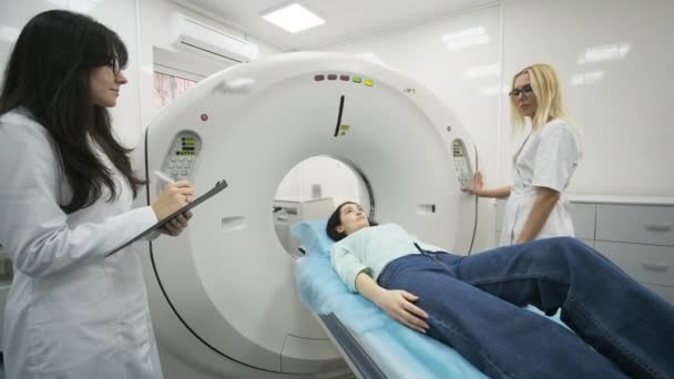 La paziente è sottoposta a TAC o risonanza magnetica sotto la supervisione di due radiologi qualificati nella moderna clinica medica. Paziente sdraiato su una TAC o una TAC, che si muove fuori dalla macchina - Filmati, video