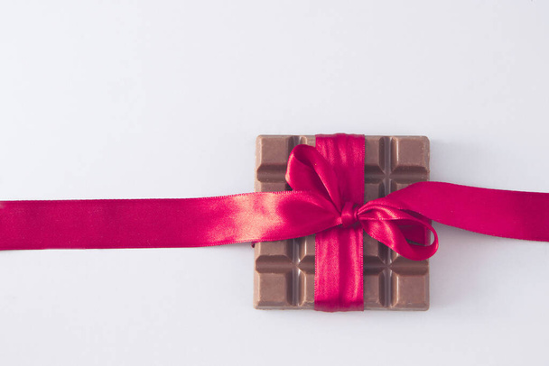 chocolate wrapped in a red ribbon in a bow. White background. Minimal composition. - Fotoğraf, Görsel