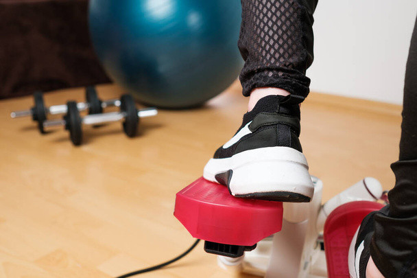 スニーカーの女性の足のバックビューは、ロックダウン中に自宅でツイストステッパーや階段のステッパーマシンで運動を行う。フィットを保つ。自宅で心臓.  - 写真・画像