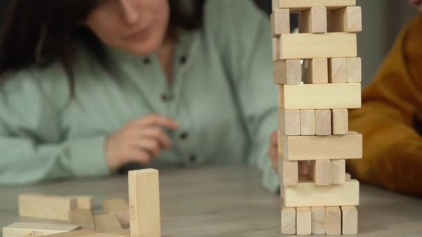 Para divertirse, una familia joven juega un juego de cubos de madera en casa. La chica saca el bloque para que la torre esté sobre la mesa.. - Metraje, vídeo