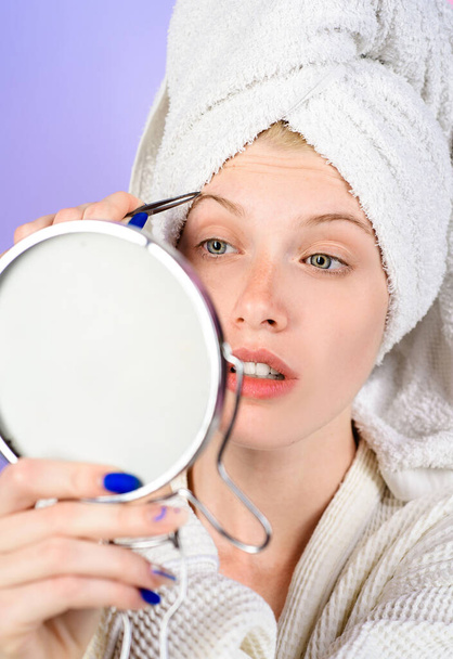Epilate Augenbrauen. Mädchen zupfen Augenbrauen und schauen in den Spiegel. Frau mit Pinzette. Kosmetik. Korrekturverfahren im Schönheitssalon. - Foto, Bild