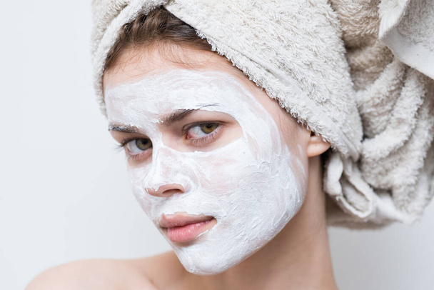 mooie vrouw met handdoek op hoofd crème masker op gezicht close-up - Foto, afbeelding