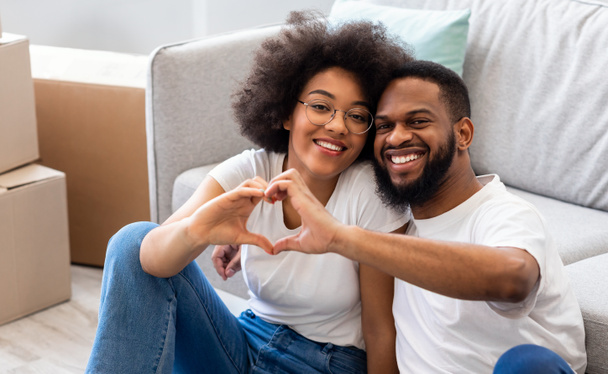 Couple assis parmi les boîtes mobiles Gesturing forme de coeur dans une nouvelle maison - Photo, image