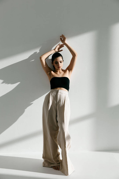 mujer con estilo en ropa de moda con los brazos levantados apoyados contra la pared de longitud completa - Foto, Imagen