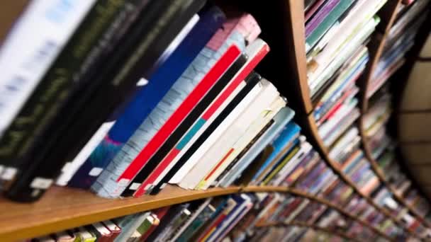 Macchina fotografica che si muove lungo scaffali curvi con libri in biblioteca - Filmati, video