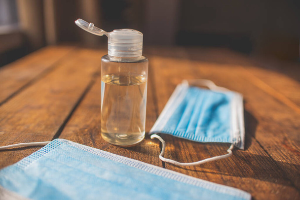пластиковая бутылка с антисептиком для рук и одноразовыми масками лежат на деревянном столе - Фото, изображение