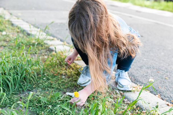 pieni tyttö vaaleat hiukset farkut ja denim takki repii pois keltainen voikukka puistossa - Valokuva, kuva