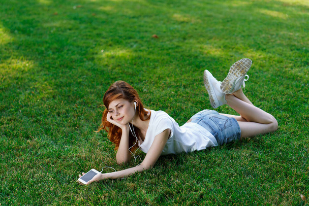 ładna kobieta leży w parku na trawniku telefon w rękach - Zdjęcie, obraz