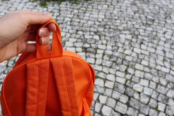 La mano femenina sostiene una mochila naranja sobre un fondo gris. - Foto, imagen