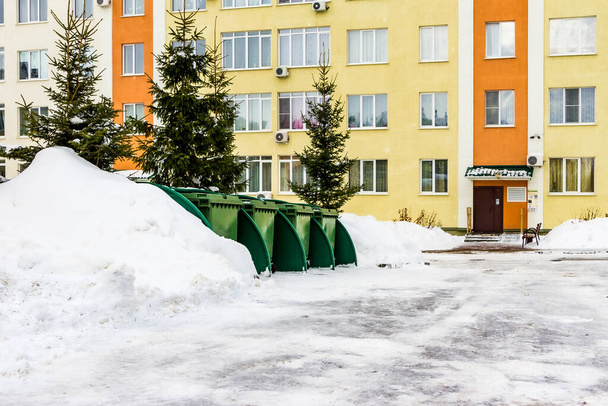 green plastic dumpsters stand between snowdrifts and Christmas trees in the courtyard of an apartment building - Photo, Image