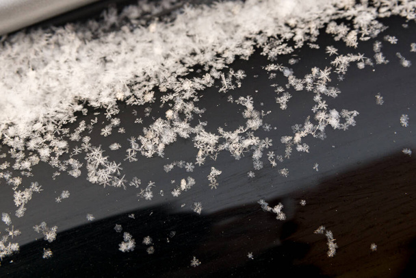 sneeuwvlokken liggen op het donkere oppervlak van het autovizier - Foto, afbeelding