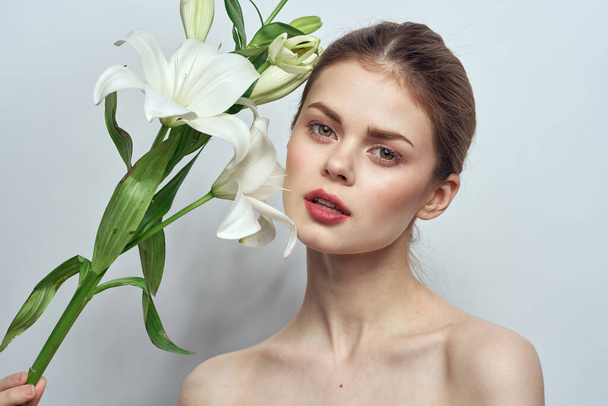 グレーの背景に白い花を持つ女性の肖像画クローズアップメイクモード - 写真・画像