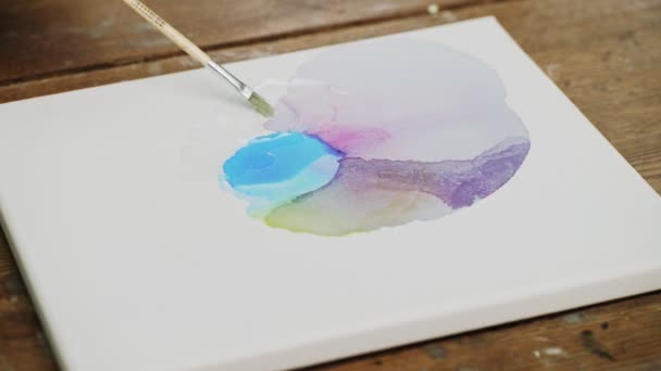 Folyékony művészet. Absztrakt színes festmény. A női művész közeli képe vizet önt a vászonra, és ecsettel terjeszti. - Felvétel, videó