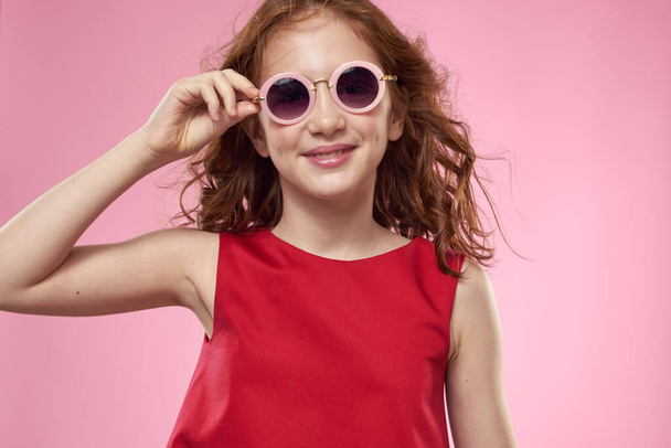Girl with curly hair dark round glasses fun red dress pink background - Foto, Bild