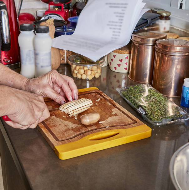 Žena připravuje recept doma v kuchyni. Seká houby na dřevěné řezací desce. - Fotografie, Obrázek