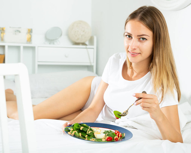 Portrait of lady eating vegetable salad in bed at home alone - Фото, изображение