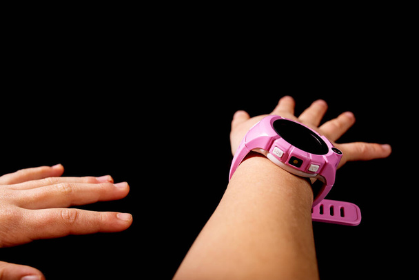 Mains d'enfant avec montre intelligente rose, isolé sur noir avec espace de copie. - Photo, image