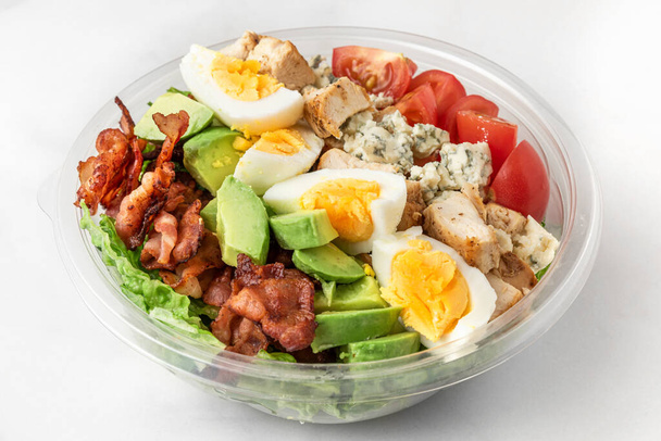 Plastic package with healthy cobb salad with chicken, avocado, bacon, blue cheese, tomatoes and eggs to take away. close up. ketogenic diet - Photo, Image