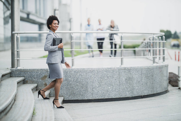 会社の建物の前の階段を歩いている間に陽気で黒人のビジネス女性. - 写真・画像