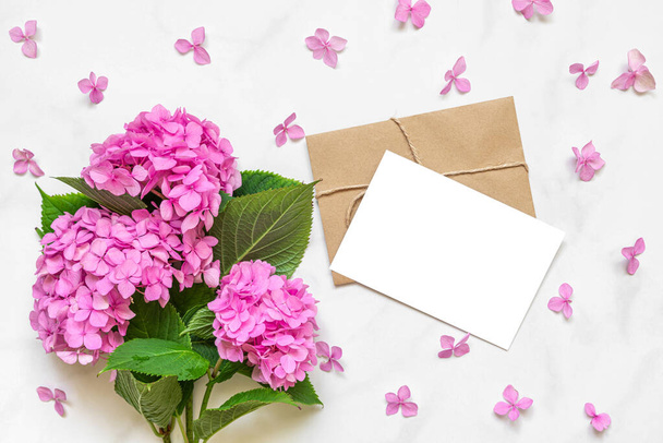 Biglietto di auguri bianco in cornice petali con ortensia rosa bouquet di fiori su sfondo bianco. Fai finta di niente. posare piatto. vista dall'alto. concetto di matrimonio o vacanza. sfondo festivo - Foto, immagini