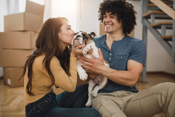 Ein glückliches junges Paar hat Spaß mit seinem englischen Bulldoggen-Welpen beim Einzug in sein neues Zuhause. - Foto, Bild