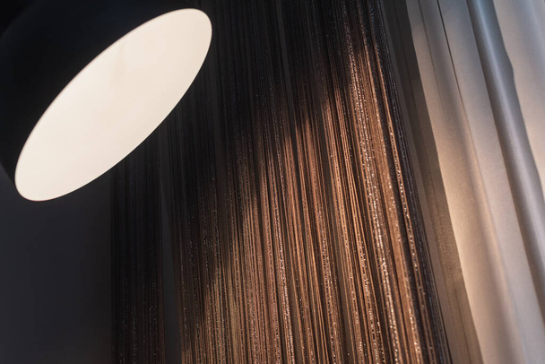 Fllor lambası koyu bej ve kahverengi perdelerin üzerine yumuşak ışık saçıyor. Seçici odak - Fotoğraf, Görsel