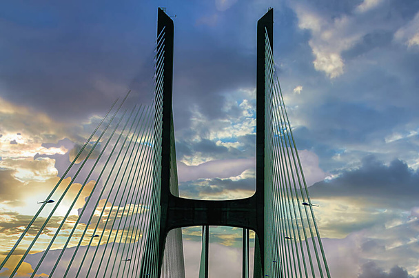 Entrée sur un pont entre colonnes et câbles avec un ciel dramatique - Photo, image