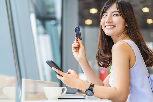 現代のコーヒーショップでオンラインショッピングのための携帯電話とクレジットカードを使用してアジアの女性,テクノロジーマネーウォレットとオンライン決済の概念,クレジットカードのモックアップ - 写真・画像