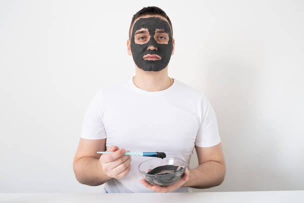 男は家で顔の皮膚の世話をする。男は粘土のマスクを顔につけた。男性の健康と美しさの概念,美容,ボディ&スキンケア. - 写真・画像