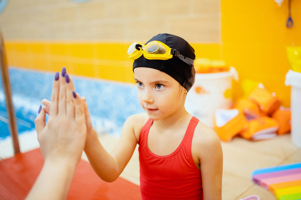 Coach geeft hand vijf aan kind meisje, concept van het leren van kinderen zwemmen in het zwembad - Foto, afbeelding