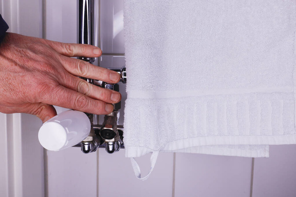 Una mano controlla la temperatura di un portasciugamani caldo in bagno. - Foto, immagini