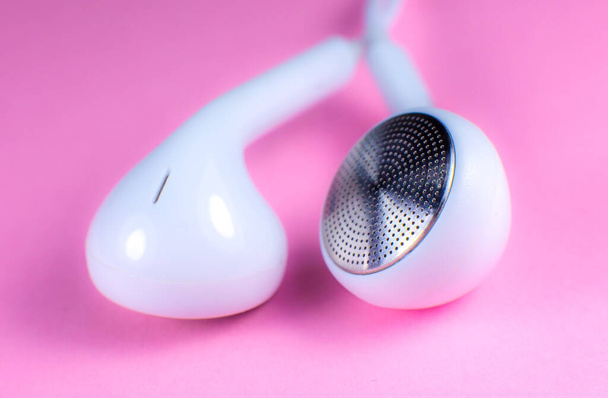 Białe słuchawki leżące na różowym tle. Koncepcja muzyki nowoczesnej. Technologia audio. Zamknij zdjęcie.. - Zdjęcie, obraz