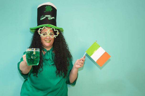 Frau mit Hut und leuchtender Shamrock-Brille und Maske von Covid 19 feiert den St. Patricks Day mit grünem Bierkrug und irischer Flagge. - Foto, Bild