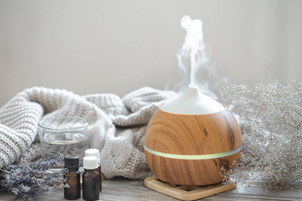 Modern aroma oil diffuser on wood surface with knitted element, water and oils in jars. - Photo, Image