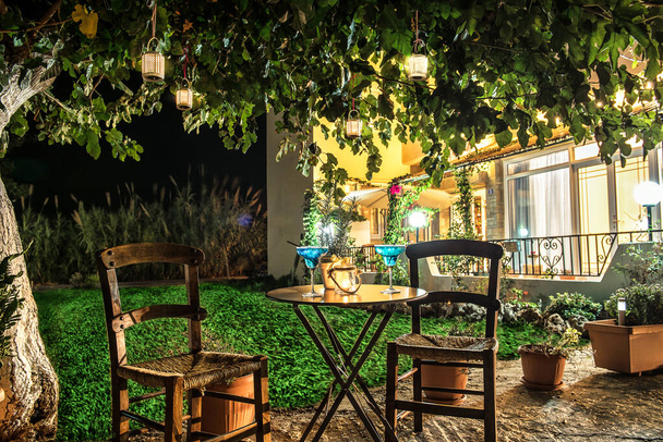 Zdjęcie z wieczornym światłem. Dwa krzesła i stół pod drzewem. Pojęcie kawiarni greckiej.  - Zdjęcie, obraz