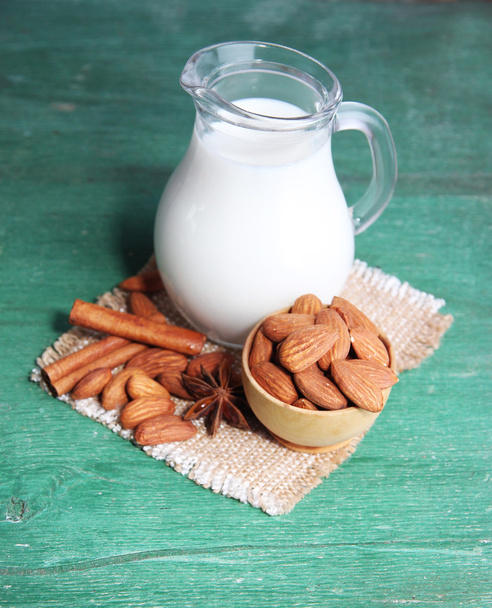 mandulás tej kancsóban mandulával csészében, színes fából készült háttér - Fotó, kép