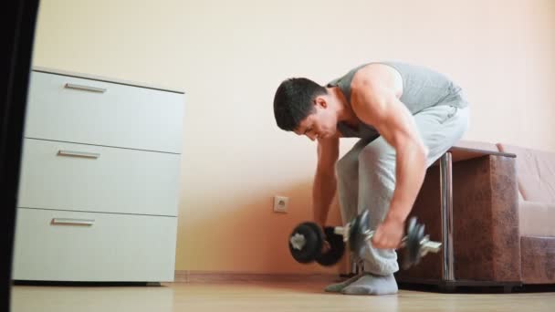 Uomo atletico muscolare che fa esercizio con i manubri a casa appoggiati sul letto. - Filmati, video