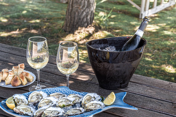 Čerstvé ústřice připravené na keramických talířích a sklenicích na víno se šampaňským na tmavém dřevě v venkovní restauraci - Fotografie, Obrázek
