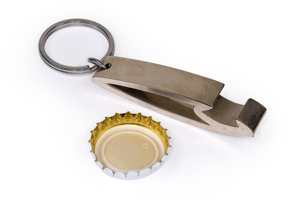 Ouvre-bouteille en métal sous la forme d'un porte-clés avec bague fendue en acier attachée et capuchon de bouteille en métal utilisé inversé avec dos en plastique gros plan sur un fond blanc - Photo, image